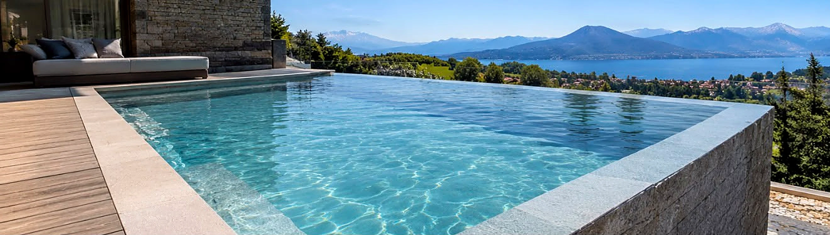 Piscina a sfioro rivestita in pietra con vista sul lago e sulle montagne
