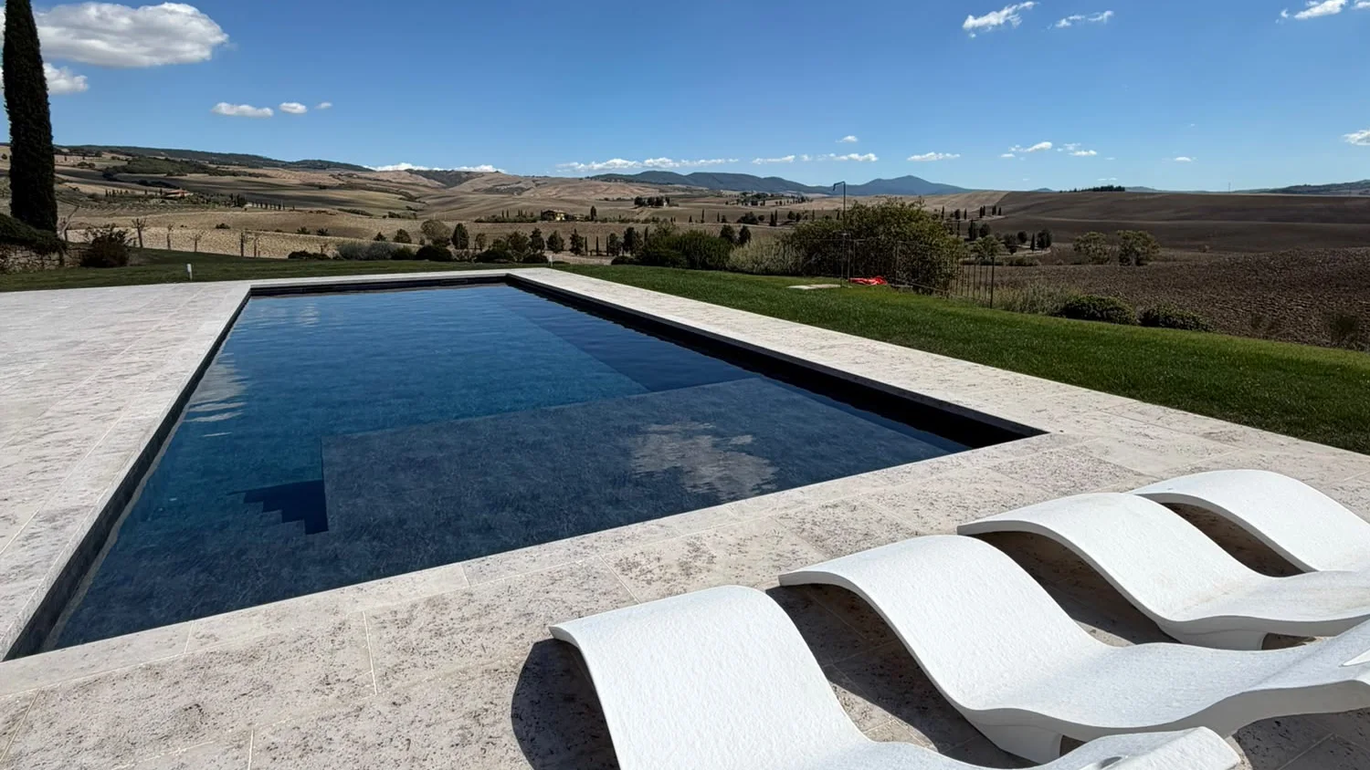 Piscina con solarium in travertino e lettini bianchi tra le colline toscane